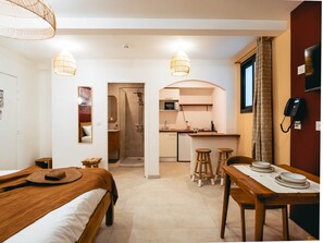 A hotel room with a bed, a small table, a kitchen area, and a bathroom. - Pointe au Sel Apartment - L'Escale Bleue, Saint-Leu, Réunion (Saint-Leu)