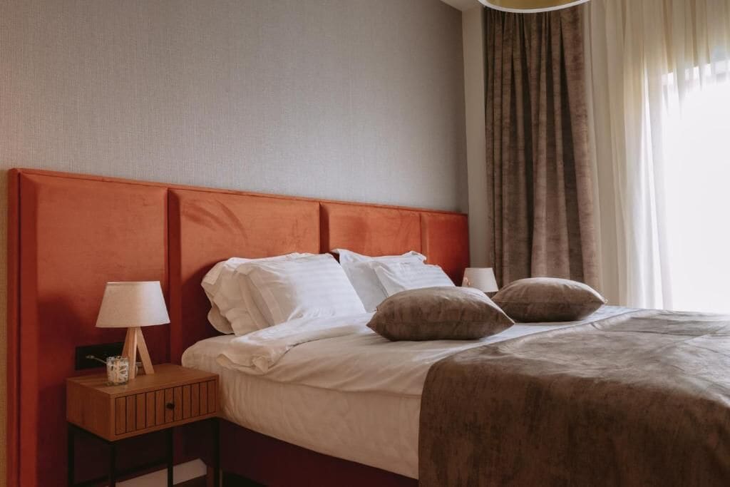 A hotel room with a bed, a nightstand with a lamp, and a window with curtains.