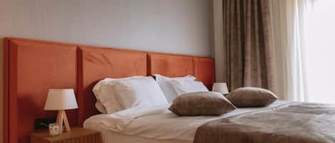 Una habitación de hotel con una cama, una mesita de noche con lámpara y un ventanal con cortinas.