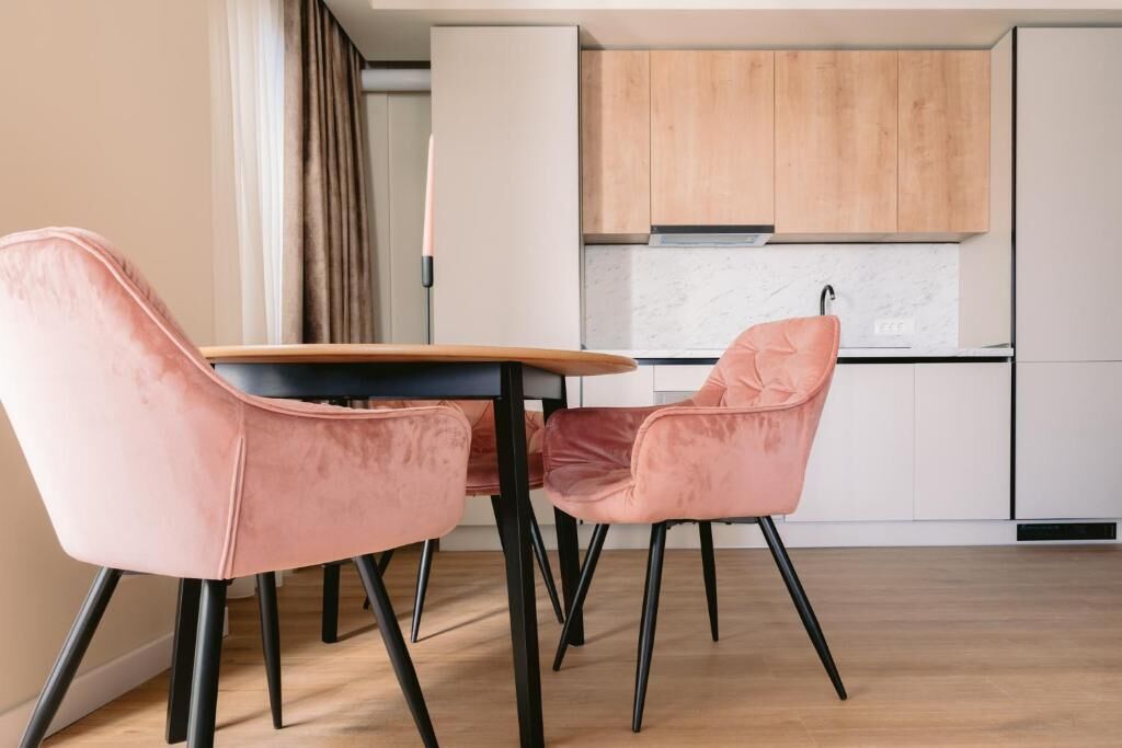 A modern kitchen with white cabinets, a wooden countertop, and a dining area with pink chairs.