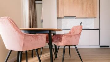 A modern kitchen with white cabinets, a wooden countertop, and a dining area with pink chairs.