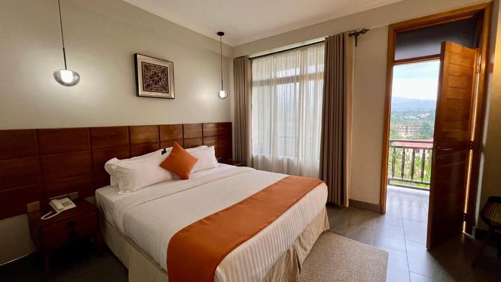Habitación de hotel con cama, mesita de noche, teléfono, ventana con cortinas y vistas al exterior.