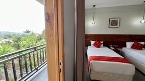 Quarto de hotel com duas camas, varanda e vista para o verde, e um ventilador de teto.