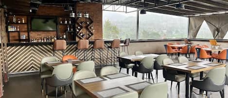 Een restaurant met een bar, meerdere tafels en stoelen, en uitzicht op het buitengebied.