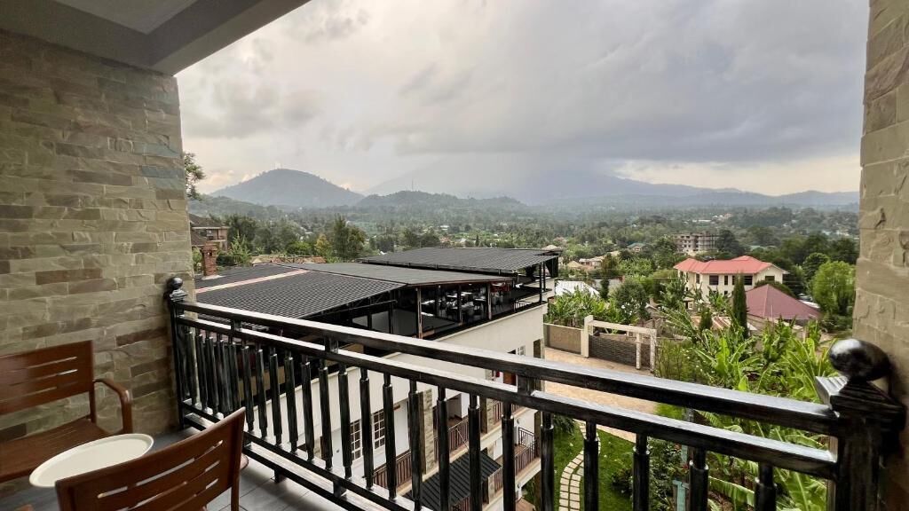 A balcony with a view of a mountainous landscape, a building with a red roof, and a stone wall.