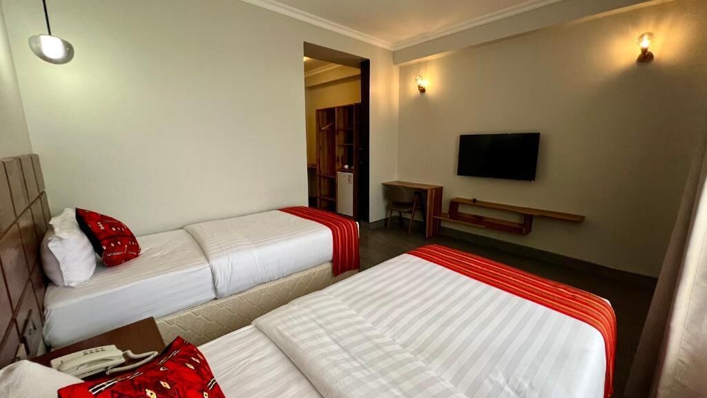 A hotel room with two beds, a desk, a television, and a wardrobe.