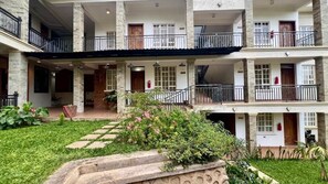 Un edificio de varios pisos con balcones, un jardín con piedras y un extintor en la pared.