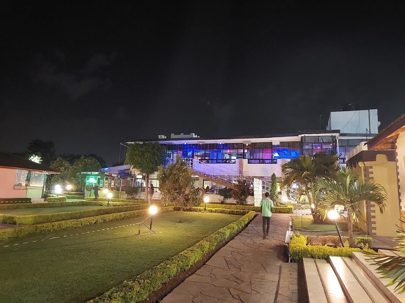 A building with a modern design, featuring a large glass facade and a well-maintained garden area with a pathway leading to the entrance.
