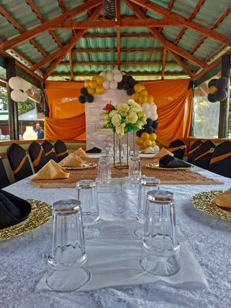 A table set for a meal with clear glasses, a centerpiece, and a backdrop of balloons and drapes.