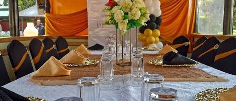 A table set for a meal with clear glasses, a centerpiece, and a backdrop of balloons and drapes.