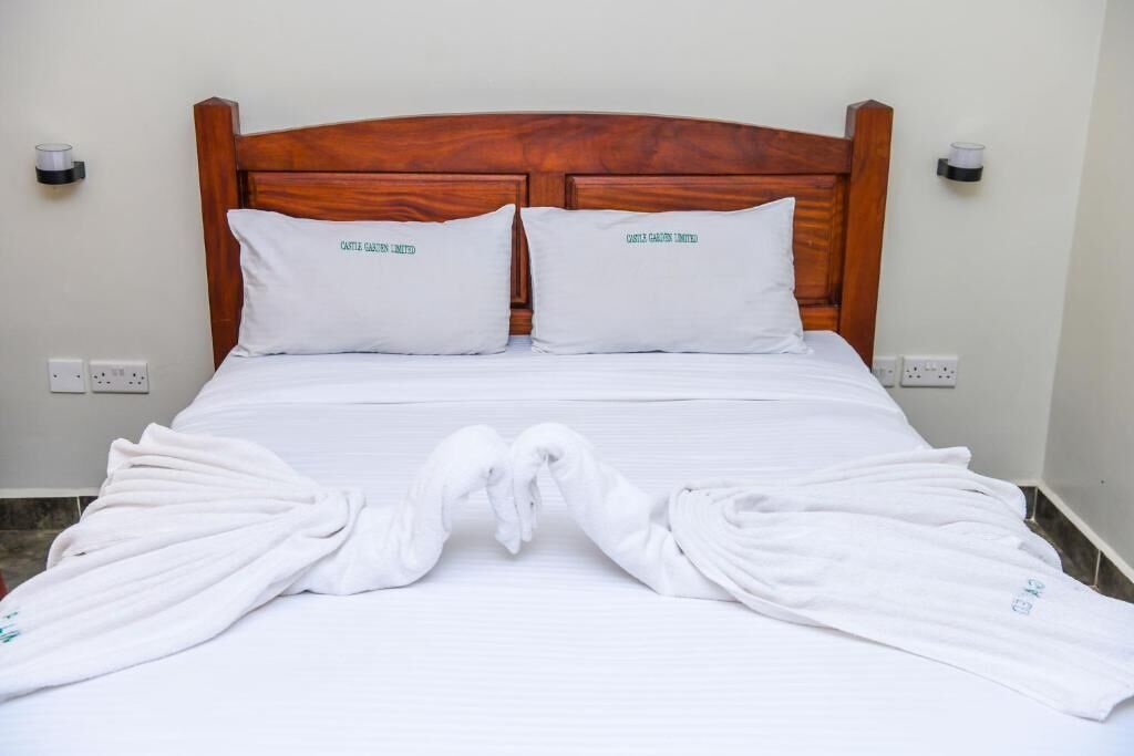 A neatly made bed with white linens and two pillows, a wooden headboard, and two bedside lamps.