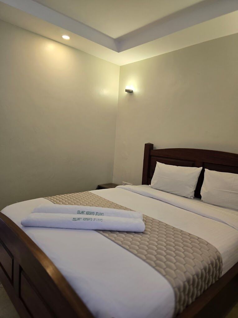 A hotel room with a neatly made bed, a headboard, and a wall-mounted light fixture.