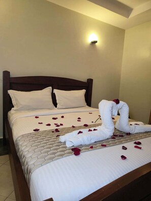 A hotel room with a neatly made bed, a headboard, and a wall-mounted light fixture. - Castle Gardens Hotel (Nairobi)