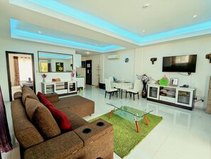A modern living room with a sofa, a glass coffee table, and a flat-screen TV mounted on the wall.