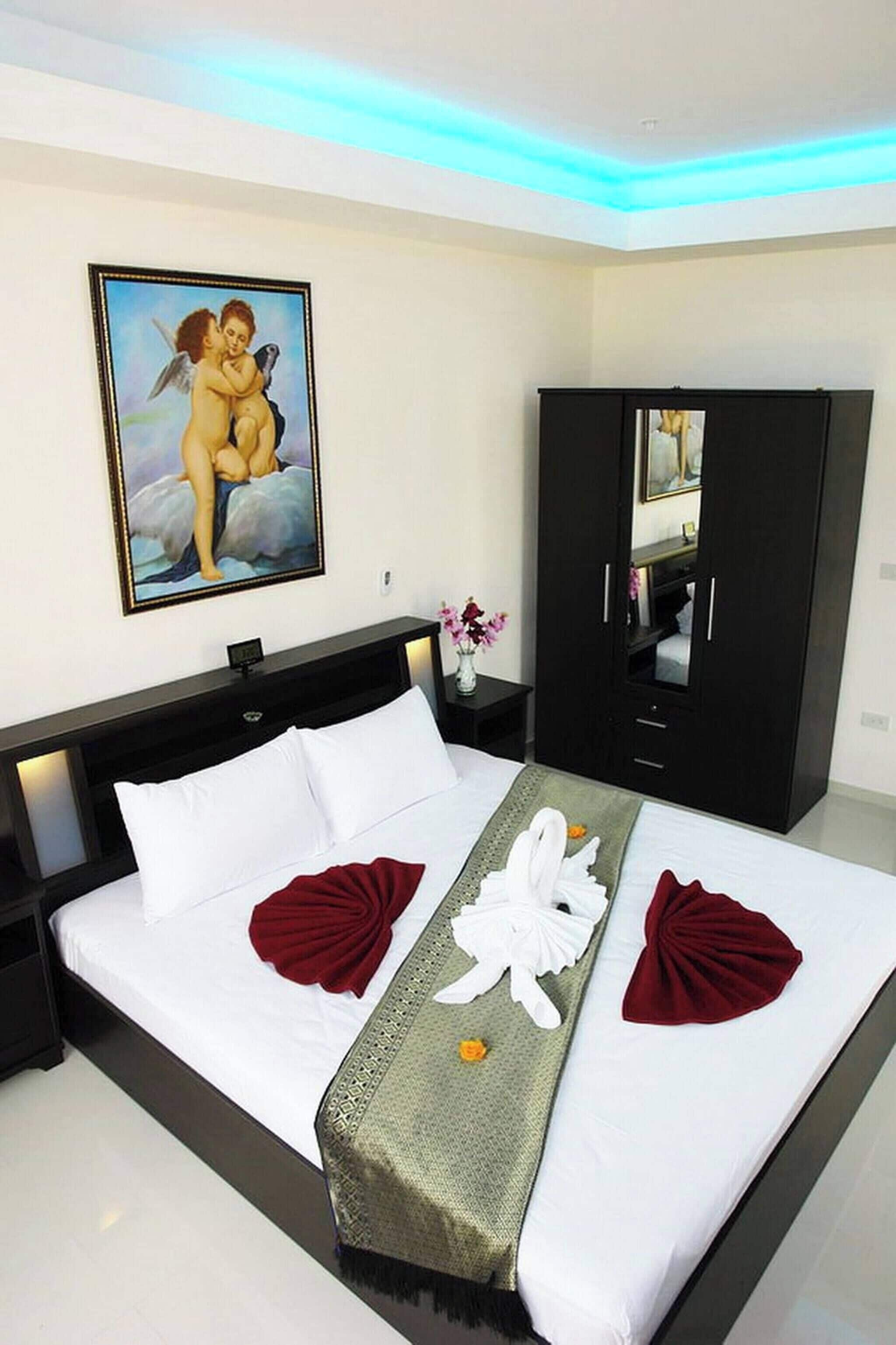 A hotel room with a bed, a nightstand, a dresser, a painting, and a vase with flowers.