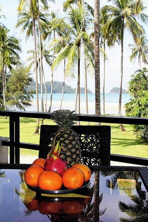 Une vue tropicale avec une table où sont présentés des fruits et une chaise.