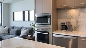 Een moderne keuken met inbouwapparatuur, een marmeren aanrechtblad en een grijze bank in de aangrenzende woonkamer.