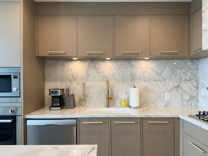 A modern kitchen with built-in appliances, a marble countertop, and wooden cabinets. - Aqua Village - Pool, Sauna, Gym, Golf Sim (Kelowna)
