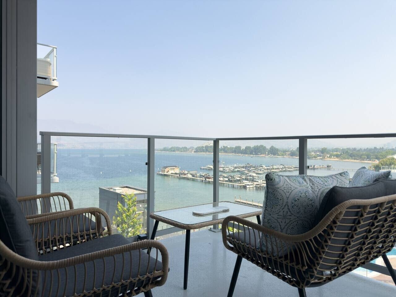 Ein Balkon mit Korbmöbeln, einem kleinen Tisch und Blick auf einen Hafen sowie Wasser.