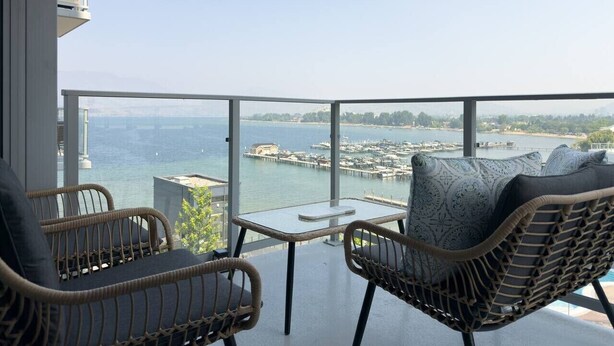 Een balkon met rieten meubels, een klein tafeltje en uitzicht op een jachthaven en water.
