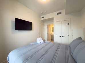 A hotel room with a bed, a flat-screen TV mounted on the wall, and a door leading to a bathroom. - Aqua Village - Pool, Sauna, Gym, Golf Sim (Kelowna)