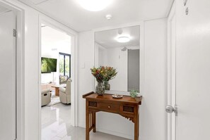 A hallway with a wooden vanity, a mirror, and a vase with flowers. - Belle Escapes 22 Rydges Plaza Esplanade with Garden Views (Cairns)