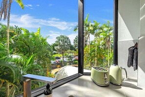 A room with a view of a parking lot and palm trees, a window with a metal railing, and a kitchenette with a toaster and kettle. - 22 Rydges Plaza Esplanade with Garden Views (Cairns)