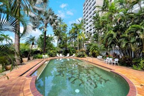 A swimming pool surrounded by palm trees and lounge chairs, with a building in the background. - Belle Escapes 22 Rydges Plaza Esplanade with Garden Views (Cairns)