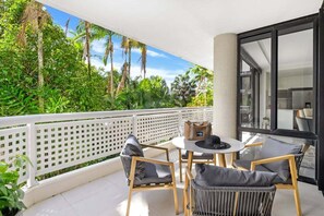 Ein Balkon mit weißem Gitterzaun, einem runden Tisch und vier Sitzgelegenheiten mit Kissen.