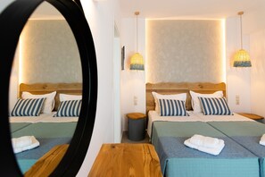 A hotel room with a large mirror, two beds with striped pillows, a wooden headboard, a small round table, and a wall-mounted lamp. - Villa in Rethymno Near Agios Pavlos Beach (Agios Vasileios)