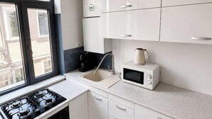 A modern kitchen with white cabinets, a gas stove, a microwave, and a window providing a view outside. - Elegant Urban Retreat | Near Old Town (Bucharest)