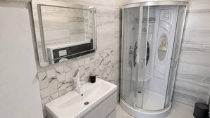 A bathroom with a white vanity, a glass-enclosed shower, and a toilet. - Elegant Urban Retreat | Near Old Town (Bucharest)