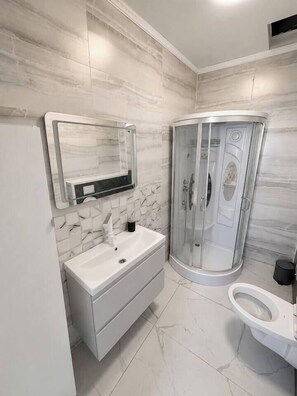 Ein Badezimmer mit weißem Waschtisch, einer Duschkabine und einer Toilette.