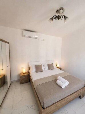 Ein Schlafzimmer mit Bett, Nachttischen, einem Spiegel und einer Klimaanlage.