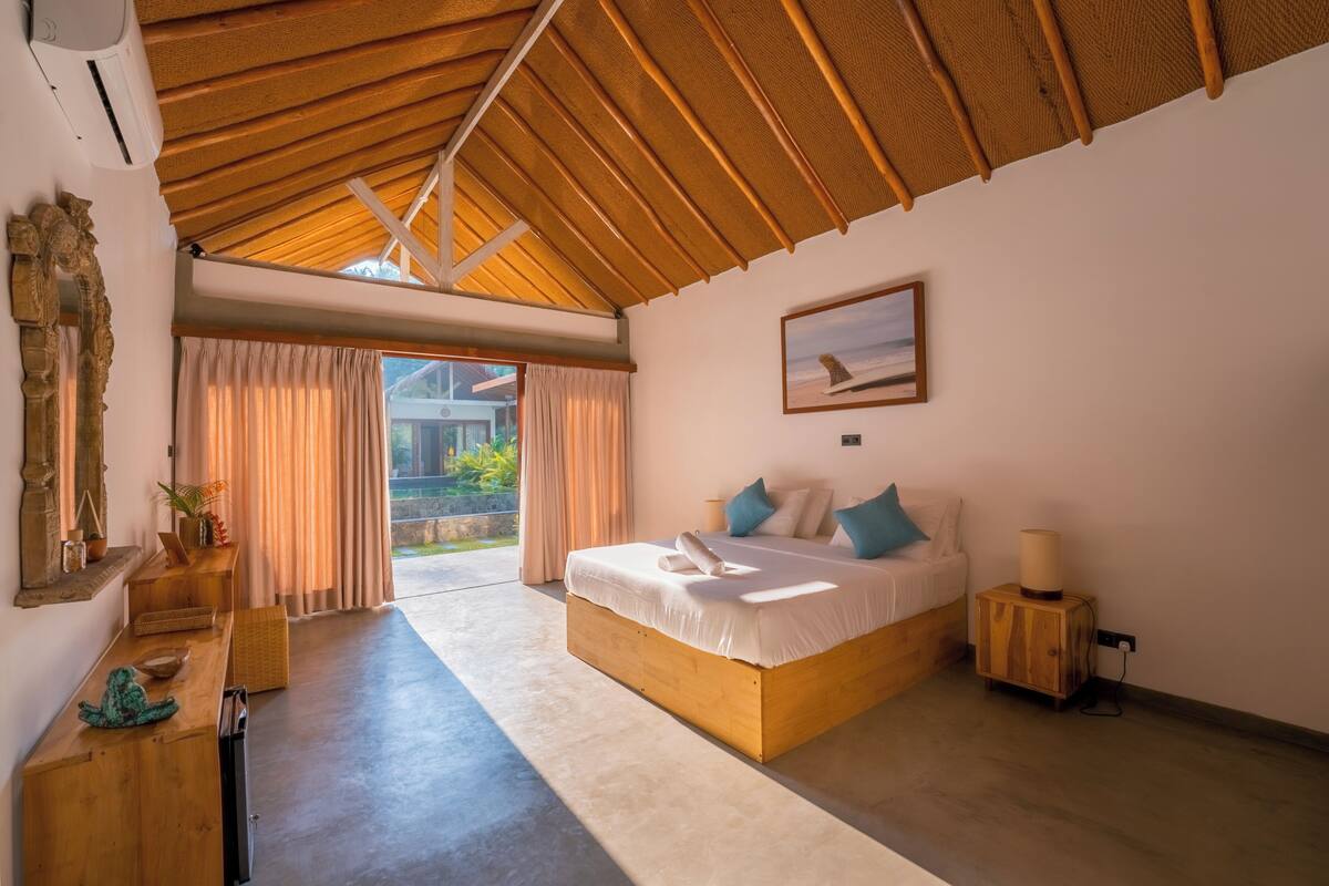 Un dormitorio con una cama grande, cabecera de madera, una mesita de noche, un espejo y vistas al exterior.