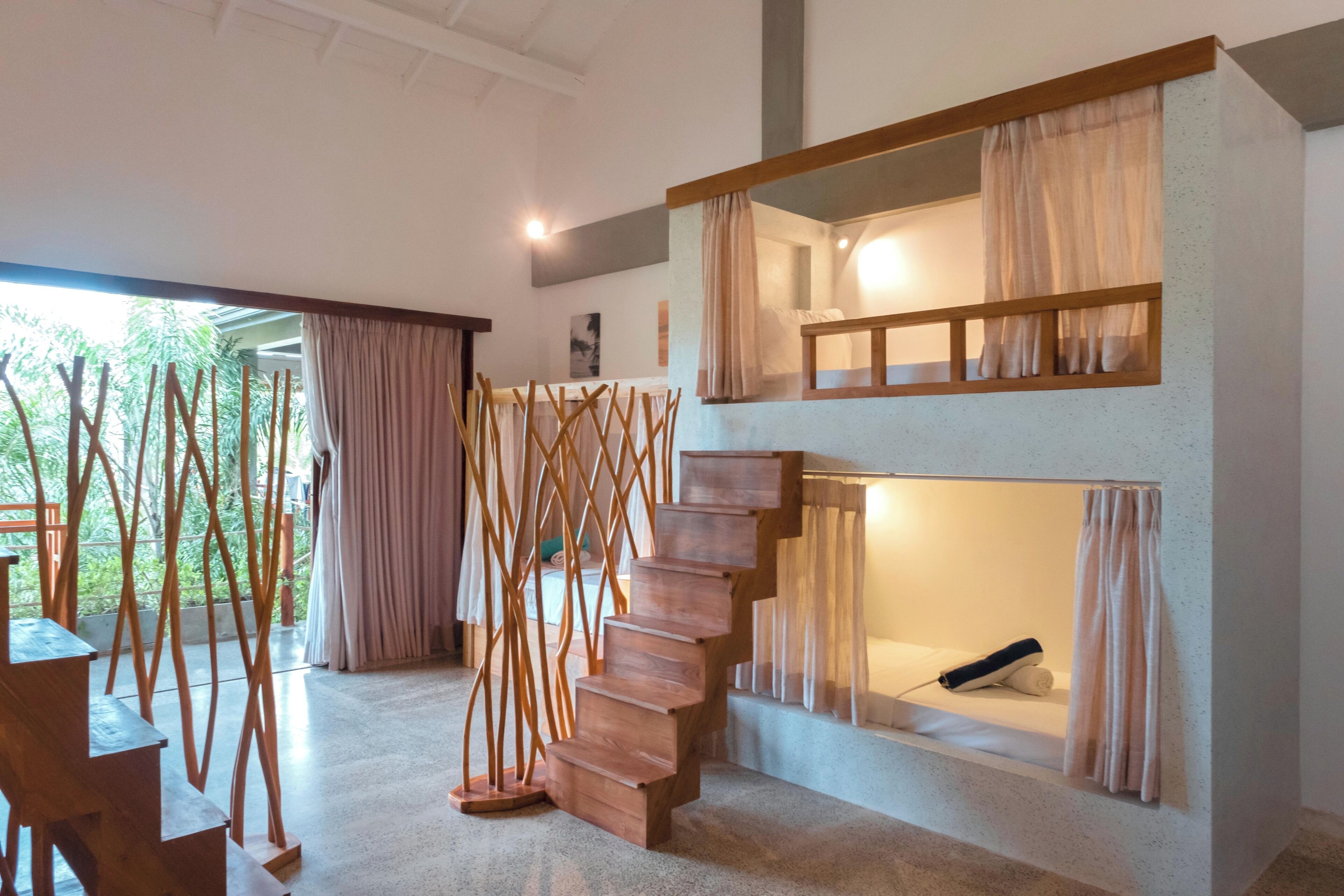 A modern interior with a staircase leading to a loft bedroom, a dining area with a view, and a large window with curtains.
