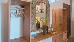 Una habitación con un armario de madera, un espejo de detalles ornamentales y una estantería con plantas decorativas y una botella.