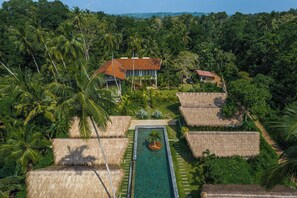 A tropical resort with a swimming pool, thatched-roof structures, and lush greenery. - Kima Surf Camp Hiriketiya (Maaliyadda)