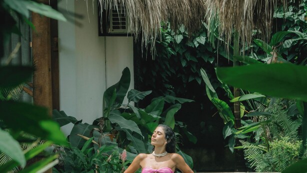 Una persona en una piscina con una estructura de techo de paja al fondo.