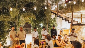 Un comedor interior con mesas y sillas, rodeado de plantas y una escalera.