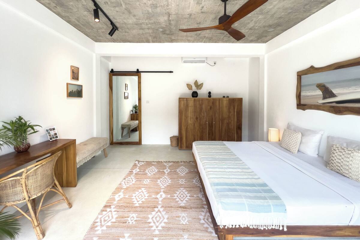 A spacious bedroom with a large bed, a wooden wardrobe, a desk with a chair, and a ceiling fan.