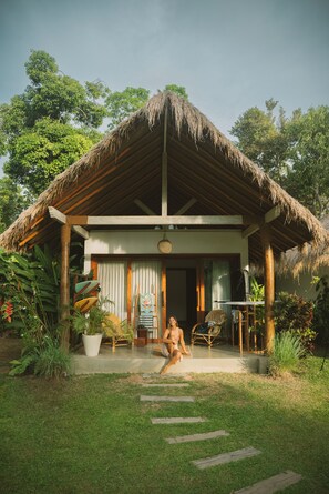 A rustic house with a thatched roof, a porch with a chair, and a potted plant. - Kima Surf Camp Hiriketiya (Maaliyadda)