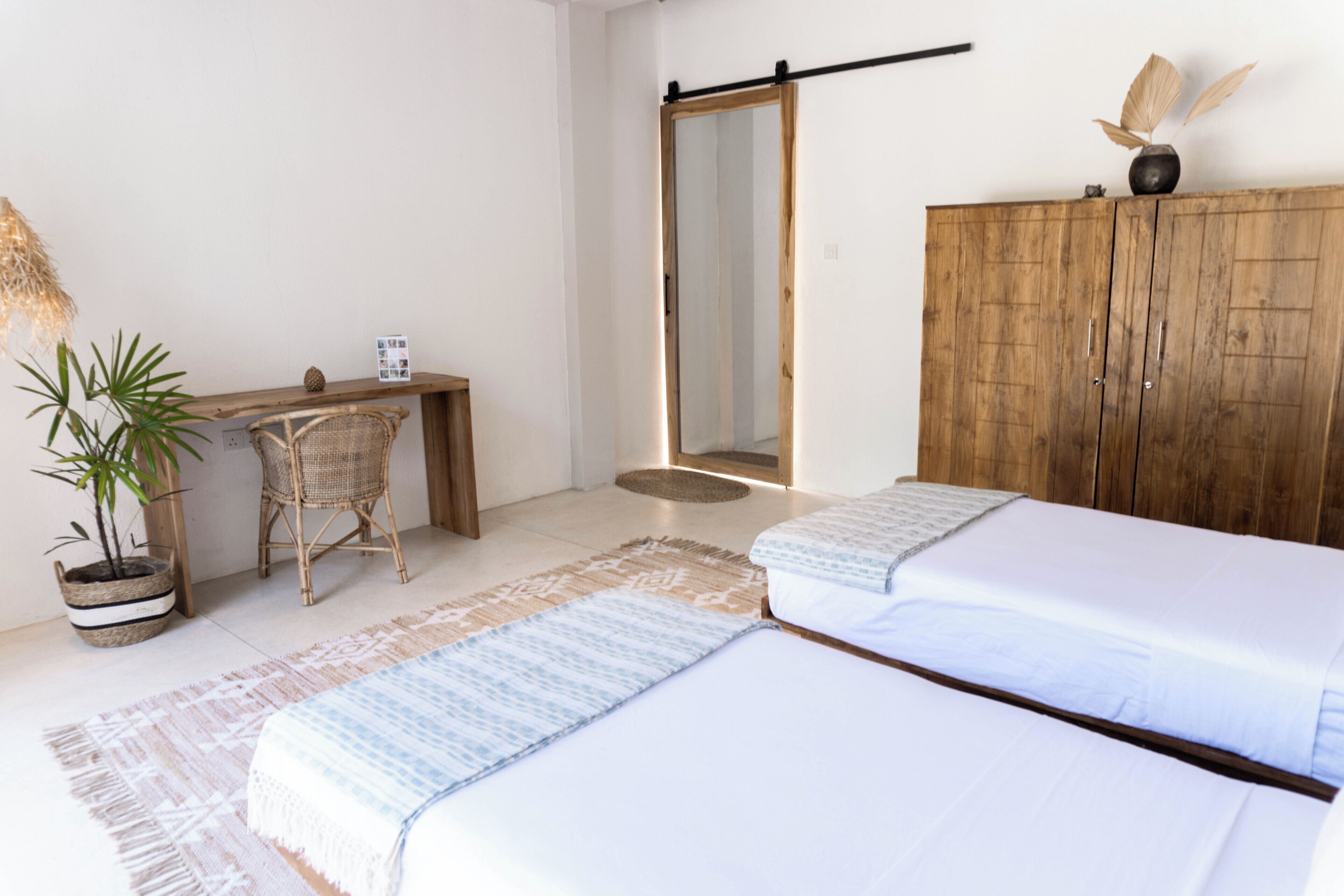 Quarto com duas camas, guarda-roupa de madeira, escrivaninha com cadeira, planta em vaso e espelho.