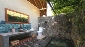 Un baño con pared de piedra, banca de madera, lavamanos y bañera.
