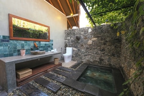 Un baño moderno con pared de piedra, lavamanos integrado, inodoro y bañera de hidromasaje.