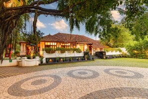 A traditional house with a tiled roof, surrounded by lush greenery and a paved driveway with circular patterns.
