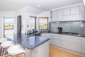 Una cocina moderna con una isla central, taburetes de bar, estufa integrada y vistas a través de las ventanas.
