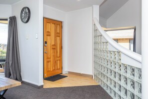 A hallway with a wooden door, a clock, and a view of a building outside.