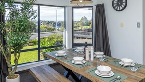 A dining area with a table set for four, a potted plant, a clock, and a view of a river and greenery outside. - Great Short-Mid Term Stay! River Views & Games Room (Hamilton)