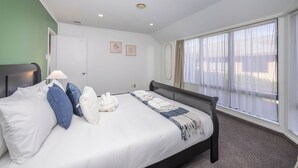 Hotelkamer met een bed, kussens, een bedlampje, een raam met gordijnen en twee ingelijste foto's aan de muur.